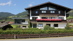 A two-story chalet with a balcony, surrounded by lush greenery and mountains in the background. - Franglhof Hohe Salve (Kirchberg in Tirol)