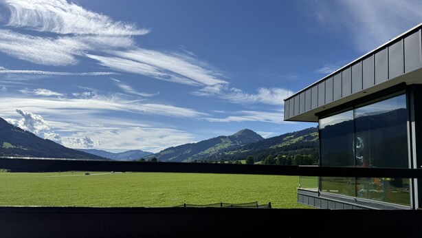 A modern building with large windows overlooking a green field and mountains. - Franglhof Hohe Salve (Kirchberg in Tirol)