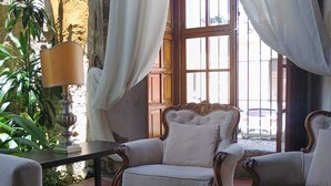Una habitación acogedora con una mesa de madera, dos sillones y un ventanal con cortinas blancas.