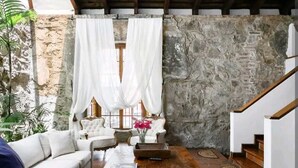 Una sala de estar acogedora con una pared de piedra, cortinas blancas, un sofá blanco y una mesa de centro de madera.