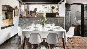 Un comedor con una mesa dispuesta para cuatro, sillas blancas, una pared de mármol y un techo rústico.