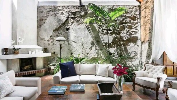 Una sala de estar con pared de piedra, un sofá blanco, una mesa de centro de madera y una planta en maceta.