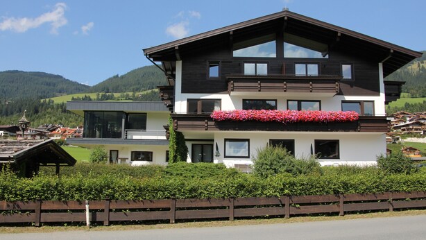 A two-story chalet with a balcony, surrounded by lush greenery and mountains in the background. - Franglhof Fleckalm in Kirchberg (Kirchberg in Tirol)