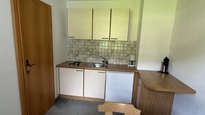 A compact kitchen with a wooden door, white cabinets, a tiled backsplash, a sink, a stove, and a coffee maker. - Franglhof Fleckalm in Kirchberg (Kirchberg in Tirol)
