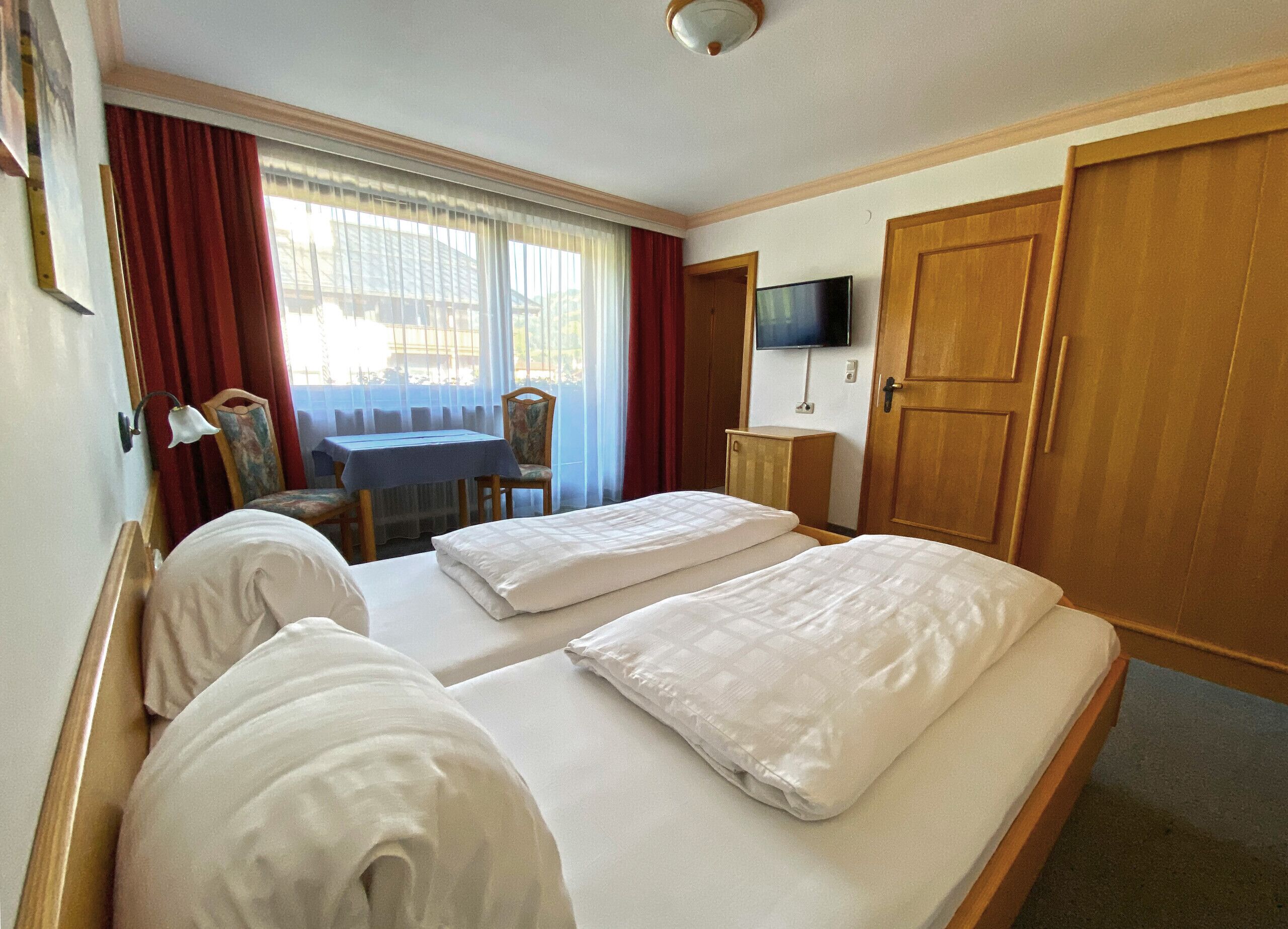 A hotel room with two beds, a desk, a chair, a TV, and a wardrobe.
