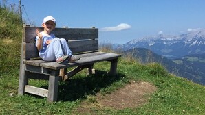 A wooden bench with a person sitting on it, overlooking a mountainous landscape. - Franglhof Fleckalm in Kirchberg (Kirchberg in Tirol)