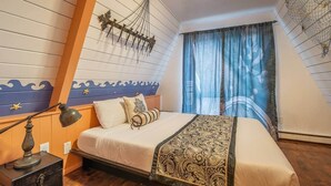 A bedroom with a sloped ceiling, a bed with a patterned bedspread, a nightstand with a lamp, and a decorative wall hanging. - Pirate 2-story Villa Near Beach (Ocean Shores)
