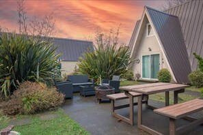 Une maison avec un toit en pente, une terrasse avec des meubles d’extérieur et un jardin où poussent différentes espèces de plantes.