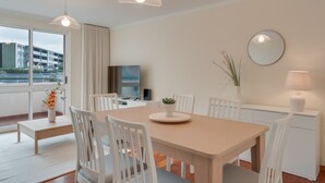 A modern dining area with a wooden table and white chairs, a TV, and a potted plant. - Funchal City Nest in Funchal (Funchal)
