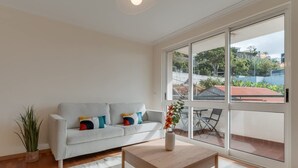 A modern living room with a white sofa, a wooden coffee table, and a large window offering a view of the outside. - Funchal City Nest in Funchal (Funchal)