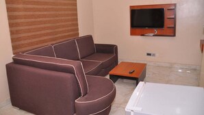 A living room with a brown sofa, a small wooden coffee table, a white side table, and a flat-screen TV mounted on the wall. - TILT APARTMENT (Bwari)