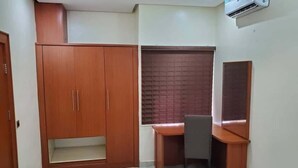 A room with a wooden wardrobe, a desk with a chair, and a brick-patterned wall. - TILT APARTMENT (Bwari)