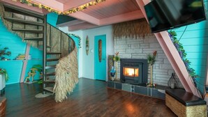 A modern living room with a fireplace, wooden flooring, a spiral staircase, and a TV mounted on the wall. - Hawaiian 2-story Beach Villa (Ocean Shores)