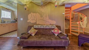 Una habitación con sofá, cojines estampados, un mural en la pared, una escalera y guirnaldas de luces.