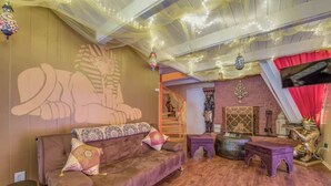 Una habitación con un mural de temática egipcia, un sofá acolchado, una mesita y una estatua decorativa.