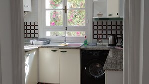 A kitchen with a washing machine, a sink, and a window with a view of pink flowers. - Yasmine Hammamet | Appartement calm and elegant (Yasmine Hammamet)