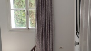 Un dormitorio con cama, ventana con cortinas, puerta y alfombra estampada.