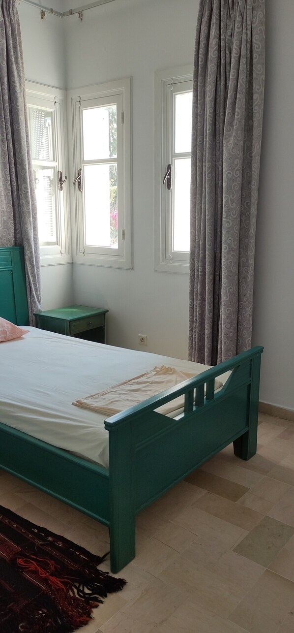 A bedroom with a bed, two windows, a nightstand, and a patterned rug.