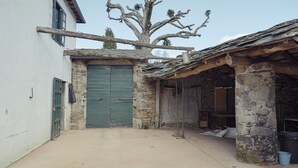 A rustic stone building with a green door, a tree with bare branches, and a sloped roof. - A Casa da Memoria - House-museum to live the experience of going back 100 years. (Aldea de Xullán)