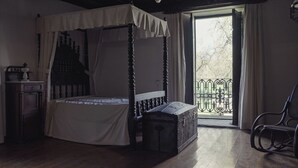 A four-poster bed with a canopy, a chest of drawers, a rocking chair, and a view of the outdoors through a balcony door. - A Casa da Memoria - House-museum to live the experience of going back 100 years. (Aldea de Xullán)