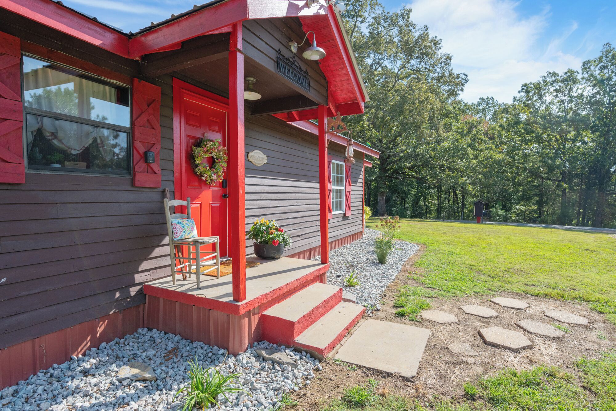 A wooden house with a red door, a porch, and a welcome sign.