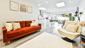 Een moderne woonkamer met een rode bank, een beige fauteuil, een wit tapijt en kunst aan de muur.
