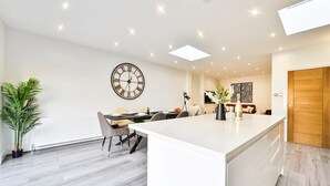 Een moderne keuken met een centraal eiland, witte kasten en een eethoek met een tafel en stoelen.