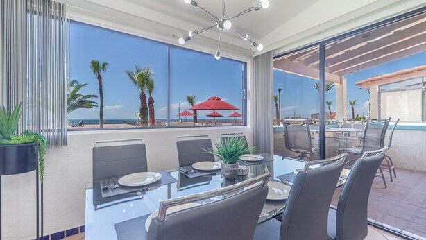 A dining area with a view of the beach, featuring a glass table, chairs, and red umbrellas. - Las Gaviotas 436 Mid-century Ocean View Apartment (Puerto Peñasco)