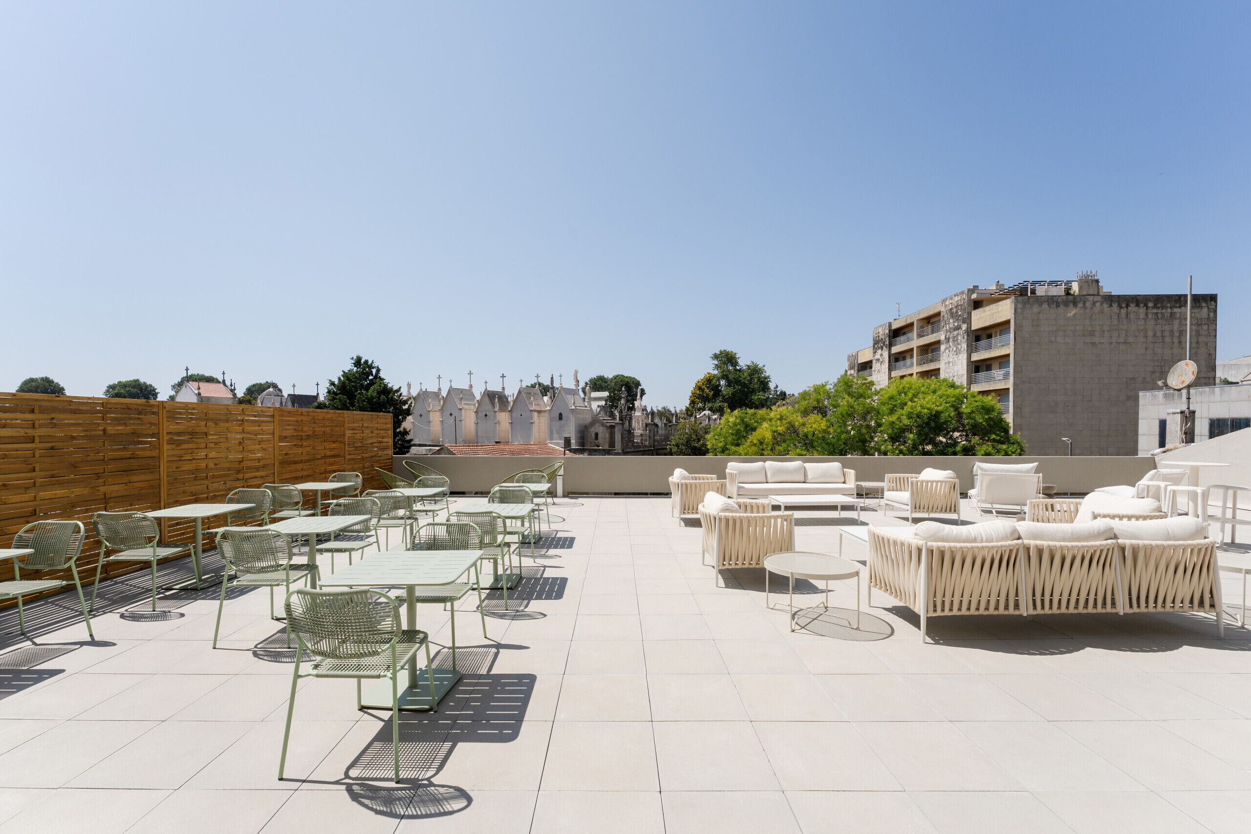 Une terrasse sur le toit, aménagée avec des espaces de détente en plein air, comprenant des tables et des chaises, et offrant une vue sur le paysage urbain en arrière-plan.