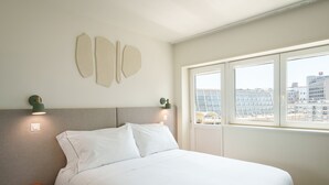 A hotel room with a bed, nightstand, wall-mounted light fixtures, and a window with a city view. - Bom Sucesso Executive Prime Studios (Oporto)
