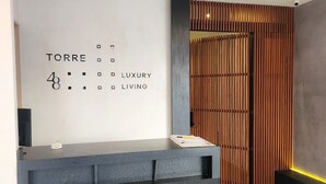 Una moderna zona de recepción con un diseño minimalista, que presenta un mostrador y un cartelito fijado a la pared con el nombre "TORRE" y la frase "LUXURY LIVING".