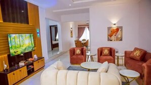A modern living room with a TV, red sofas, and a white sofa. - TAJ SUITES  (Ado Ekiti)