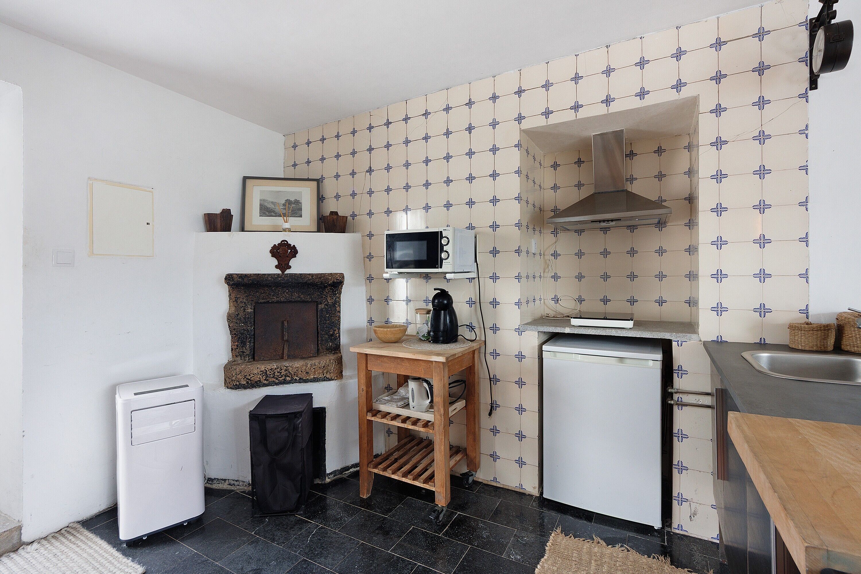 A compact kitchen with a microwave, a small refrigerator, a sink, and a wooden shelf.