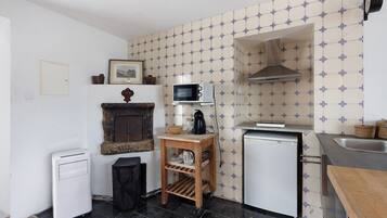A compact kitchen with a microwave, a small refrigerator, a sink, and a wooden shelf.