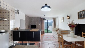 Et moderne køkken med en central ø, et spiseområde med træstole og udsigt gennem en glasdør til en udendørs balkon.