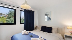 Et hotelværelse med en seng, et natbord, en lampe, et vindue med gardiner og et billede på væggen.