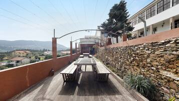 A wooden deck with picnic tables, a stone wall, and a building with large windows in the background.