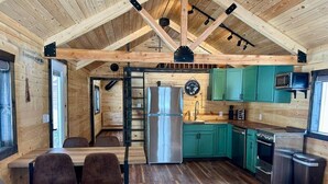 A rustic cabin interior with a wooden ceiling, a dining area with chairs, a kitchen with green cabinets, and a stainless steel refrigerator. - Index Peak Cabin (Silver Gate)