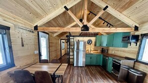 A cabin interior with a wooden floor, a dining area with two chairs, a kitchen with green cabinets, a stainless steel refrigerator, and a microwave. - Index Peak Cabin (Silver Gate)