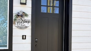 Une porte d’entrée noire avec une petite fenêtre, une boîte aux lettres et une guirlande décorative.