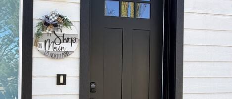 A black front door with a small window, a mailbox, and a wreath sign.