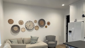 Un salon moderne comprenant un canapé, des fauteuils, une table basse et un coin cuisine avec un réfrigérateur.