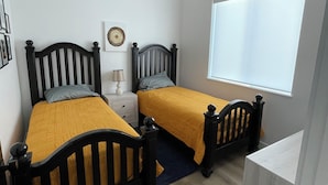 Une chambre avec deux lits simples, un ventilateur de plafond, une fenêtre et une table de chevet avec une lampe.