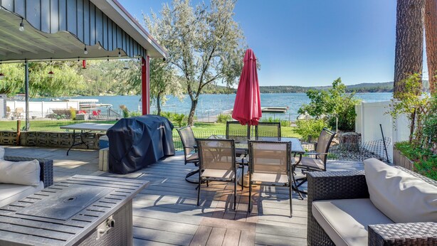 An outdoor deck with a table and chairs, a red umbrella, and a view of a lake. - Waterfront Deck w/ Fire Pit: Lake Spokane Gem! (Nine Mile Falls)