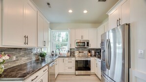 A modern kitchen with white cabinets, stainless steel appliances, and a marble countertop. - Waterfront Deck w/ Fire Pit: Lake Spokane Gem! (Nine Mile Falls)