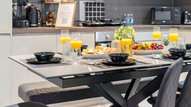 Una cocina moderna con una mesa de desayuno dispuesta, mostrando jugo de naranja, pastelería y un frutero.