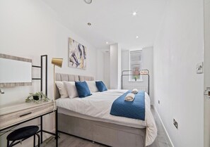 A modern bedroom with a bed, desk, and a window.