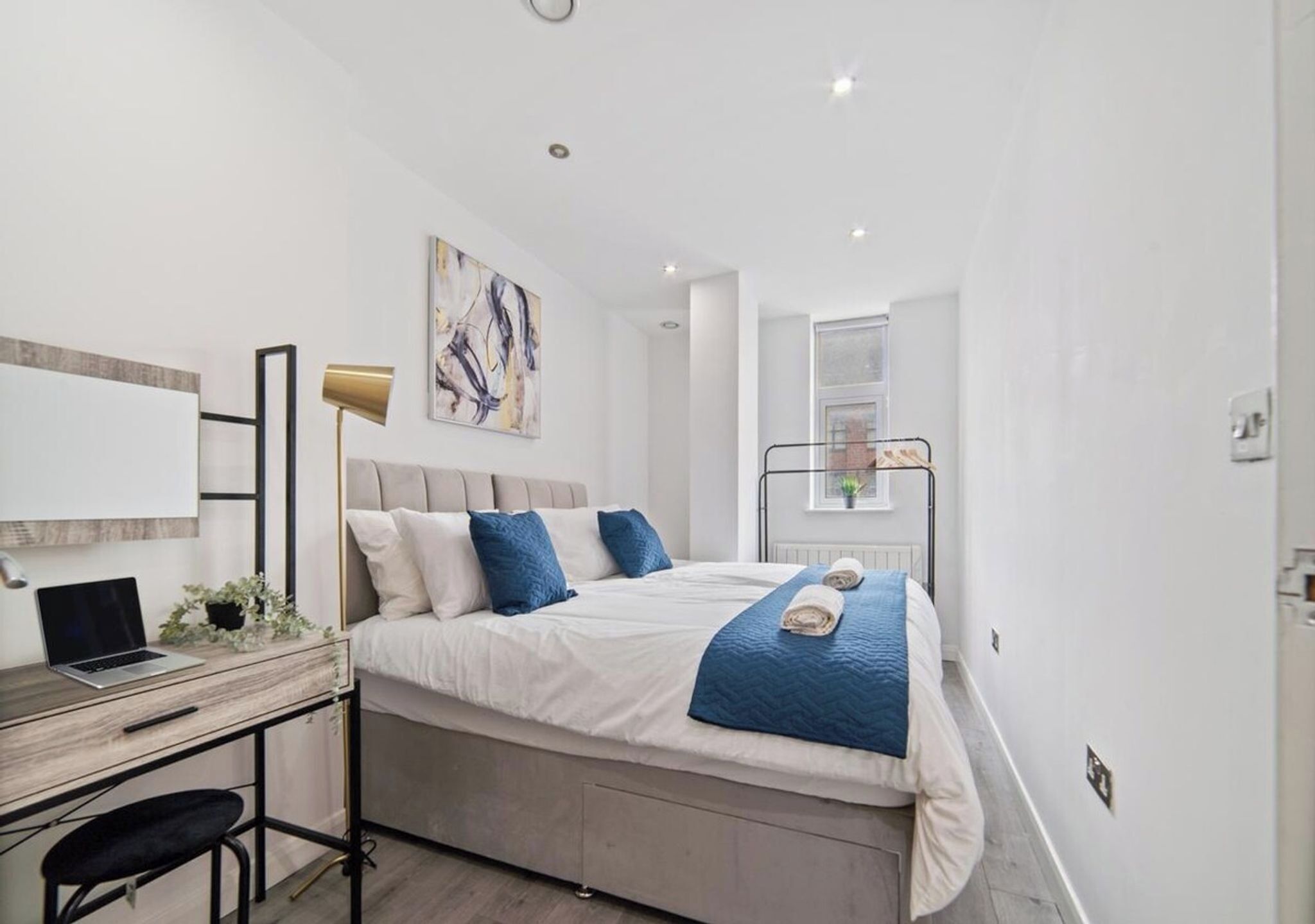 A modern bedroom with a bed, desk, and laptop.