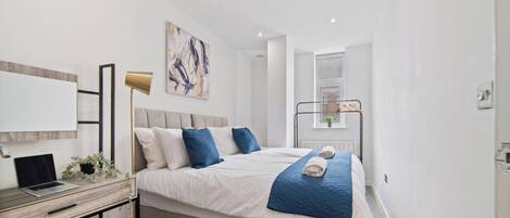 A modern bedroom with a bed, desk, and laptop.