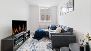 Una sala de estar moderna con un televisor de pantalla plana, un sofá gris y una alfombra azul.